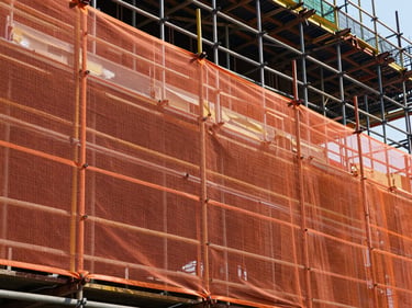Side view of perimeter safety netting and guardrail system installed on a multi-story building under construction, daylight, orange safety net taut between scaffold uprights