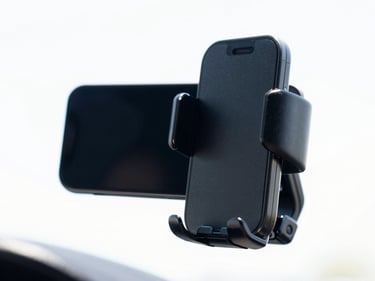 Close-up of a black car phone mount gripping a smartphone, mounted on a car dashboard, clean white background, bright high-key product photography, crisp natural daylight, vivid colors, sharp focus, 35mm