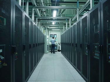 Wide shot of a modern data center cooling plant, visible pipes and chillers, cool industrial lighting, engineer reviewing a control panel in the mid-ground.