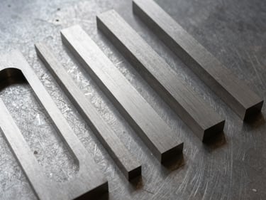 Overhead flat-lay of freshly laser-cut stainless steel parts arranged on a dark steel surface, raking side light revealing sharp cut edges and surface texture, varying thicknesses visible