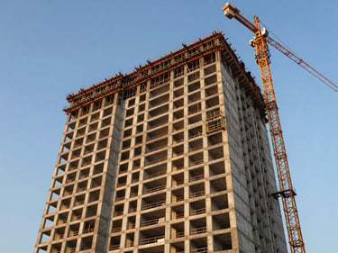 Ground-level view of a premium pre-launch residential tower under construction in Mohali, concrete frame visible against clear blue sky, cranes in background, golden afternoon light on facade