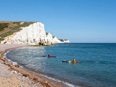 Scenic view of Swanage Bay with kayakers paddling near the chalk cliffs, rich ocean blues, bright sunny day.