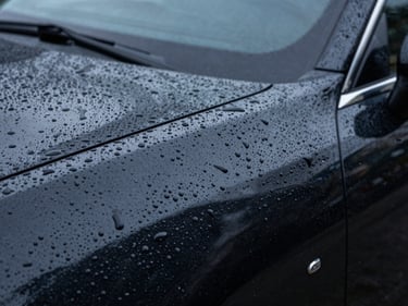 Close-up of water beading on ceramic-coated deep black car paint under cool studio lighting, sharp droplets standing tall on a mirror-smooth surface