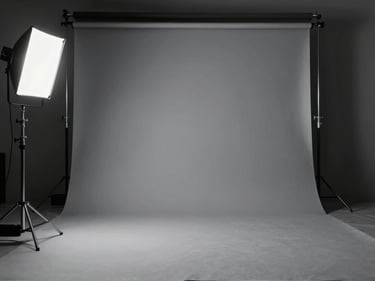 Wide environmental shot of an empty photography studio with a grey seamless backdrop, a lighting rig and C-stand in the foreground, silver key light on the left, deep shadow on the right side of the frame, no people