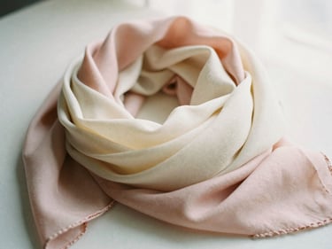 Softly folded pastel pink and cream scarves layered together under diffused window light, 35mm