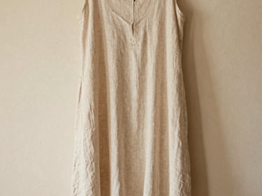 Editorial shot of a flowing beige linen dress hanging against a warm plaster wall, soft natural light, 35mm