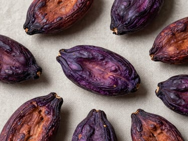 Overhead flat-lay of raw fermented cacao beans arranged on a neutral linen surface, studio strobe from above showing color gradation from deep purple to mahogany — no styling, no garnish, macro detail of bean surface texture