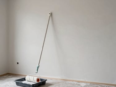 Wide shot of a freshly painted interior wall in a light neutral tone, paint roller resting on a tray in the foreground, bright ambient daylight, no people visible