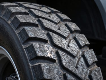 Close-up of deep commercial truck tire tread patterns, high-contrast industrial lighting, steel grey tones.