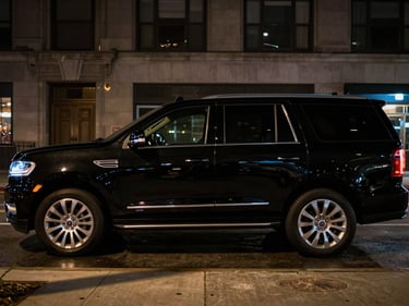 Night-time cinematic profile of a glossy black Ford luxury SUV staged on a wet Chicago street, building glow catching the chrome door trim, shot from pavement level, no passengers, deep shadow in background