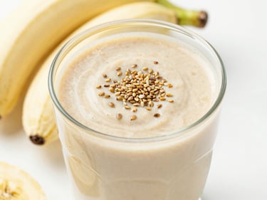 Creamy almond butter and banana smoothie topped with hemp seeds, bright high-key lighting, clean slate background