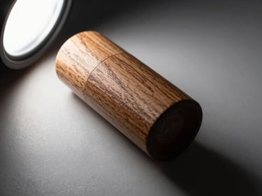 Extreme close-up of a premium product on a matte surface, a single studio strobe raking across the object from the upper left, deep shadow on the right, minimal background, rich texture and material detail in sharp focus