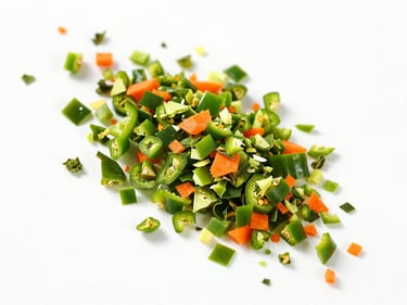 High-key overhead shot of dehydrated green bell pepper flakes and carrot granules on a clean white surface.
