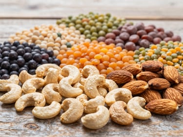 Assortment of colorful pulses and dry fruits (cashews, almonds) on a rustic wooden surface, bright natural daylight, rich organic tones, high detail, 35mm