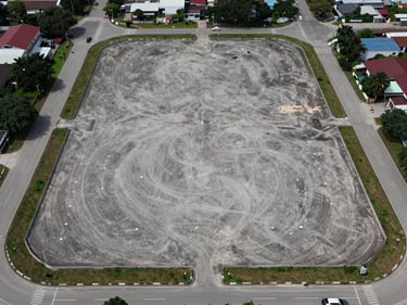 Straight-on aerial view of a cleared industrial land parcel in Johor Bahru, flat lot with boundary markers visible, surrounding road access, overcast natural daylight, no people