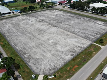 Overhead diagonal aerial view of a large vacant industrial land parcel in Johor Bahru with clearly marked boundary fencing, surrounding roads visible, overcast daylight