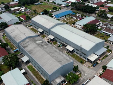 Overhead diagonal aerial perspective of a semi-detached factory cluster in Johor Bahru, rooftops and yard space visible, surrounding industrial estate context, natural daylight, no people