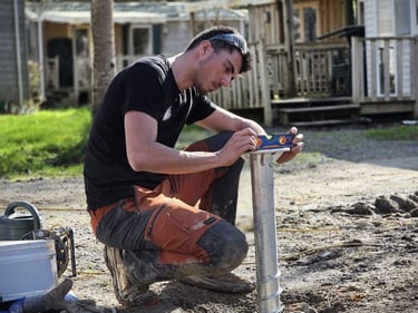 A worker using a spirit level to check the alignment of a ground screw foundation pile for a construction project.