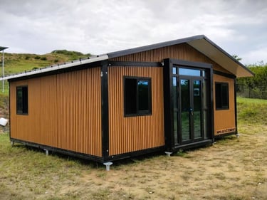 Modern prefabricated modular cabin with wood slat siding and black window frames in a rural landscape.