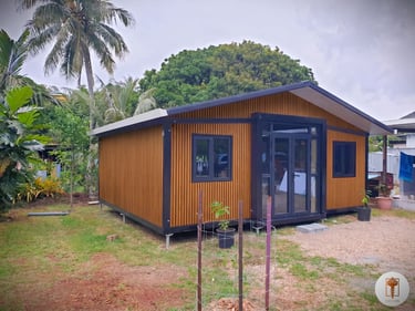 Modern wood-paneled tiny home or modular cabin with black trim nestled in a tropical landscape.