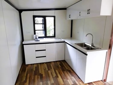 Modern tiny house kitchen with white cabinets, wood flooring, and a stainless steel sink.