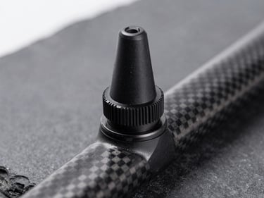 Sleek black tubeless valve stem mounted on a deep-section carbon rim, macro depth of field