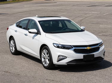 Three-quarter front view of a clean 2020 Chevrolet Malibu in pearl white on a bright outdoor lot under even daylight, neutral asphalt background, no people
