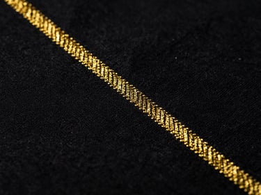 Macro detail shot of heavy black cotton fabric with metallic gold embroidery thread, high contrast dark lighting.