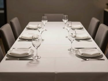 Wide-angle view of a polished corporate dinner table set for twelve, crystal glassware and white linen, soft directional light from above, no people present