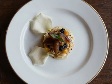 Close overhead view of an elegantly plated wedding dinner course on white porcelain, gold-rimmed charger plate, single white rose petal beside the arrangement, soft studio light