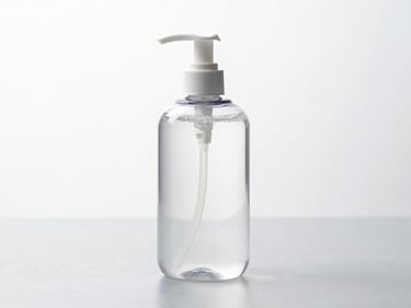 A clear handwash bottle with a pump dispenser on a reflective light grey surface, sharp focus.