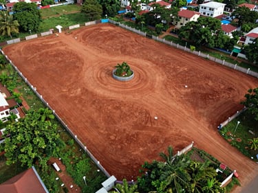 Aerial drone shot of open residential plots in a gated community layout near Vizianagaram, boundary markers visible, red laterite soil, surrounding greenery
