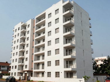 Wide shot of a modern residential apartment block in Visakhapatnam's MVP Colony, natural daylight, clean concrete facade with balconies, street-level context visible