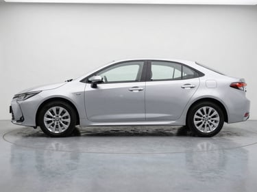 Side-on full view of a silver Toyota Corolla on a grey studio floor, natural overcast daylight, clean white background, showing true body finish