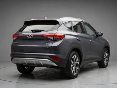 Three-quarter rear view of a dark grey Hyundai Tucson on a neutral grey studio floor, even diffused light showing rear lights and bumper detail