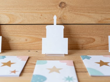 Styled flat lay of custom event decor including a cake topper, small acrylic sign, and personalized party favors, with stars and organic shapes, bright natural light, warm wood backdrop, scrapbook style