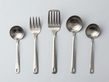 Industrial stainless steel kitchen utensils laid out on a clean gray background, top-down flat lay