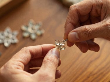 Macro photograph of hands carefully threading tiny glass beads into a complex floral pattern, warm indirect daylight, shallow depth of field.