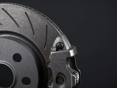 Macro close-up of a ventilated brake disc rotor edge and caliper bracket on a dark matte background, dramatic side-lighting emphasizing cast iron texture and venting slots