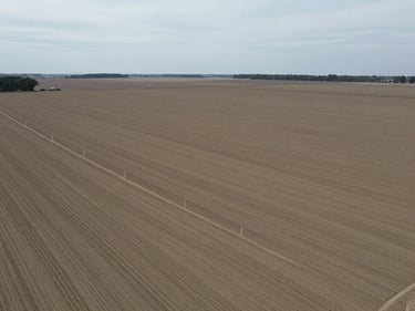 Wide-angle drone shot of raw acreage with clear boundary markers, overcast daylight, desaturated tones