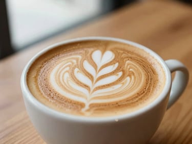 Close-up of a freshly poured latte with delicate leaf latte art on a warm wooden table, soft window light