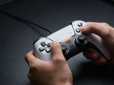 Hands gripping a game controller in low-key side-light, reflective chrome triggers catching a narrow amber beam, deep shadow on matte black background, extreme close-up framing isolating fingers and hardware detail