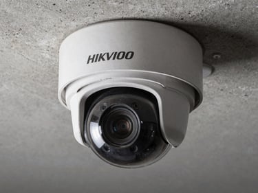 Close-up of a Hikvision PTZ dome camera mounted on a concrete ceiling bracket, steel housing detail visible, cool studio strobe lighting, no people