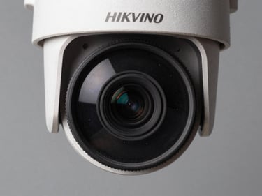 Extreme closeup of a Hikvision PTZ bullet camera body, lens housing centered, neutral studio strobe, steel-gray background, no text