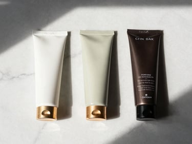 Flat-lay of three hair care product tubes arranged in a routine sequence on white marble, natural light from above, gold accents on caps, no text