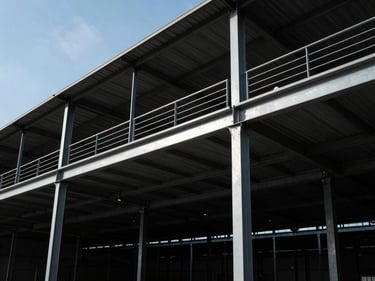 Industrial mezzanine structure with steel beams, showing an upper level for storage or offices, wide-angle shot, high-contrast industrial daylight.