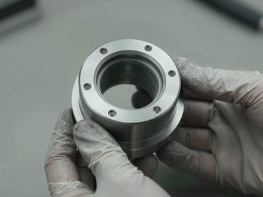 Finished machined part held in gloved hands for inspection under task lighting, surface coating visible and uniform, plain bench background