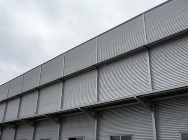 Wide-angle exterior of an industrial facility building facade under overcast light, metal cladding panels and structural elements visible, no people, technical environmental framing