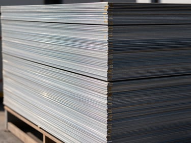 Side-on close-up of MS plates stacked in a neat pile on a loading dock, edge markings visible, high-contrast work-light illumination showing surface flatness and thickness variation