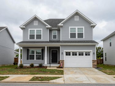 Wide shot of a newer two-story home in Rogers AR, light grey siding, front porch, quiet street, even overcast daylight, real neighborhood context with neighboring homes visible at the edge